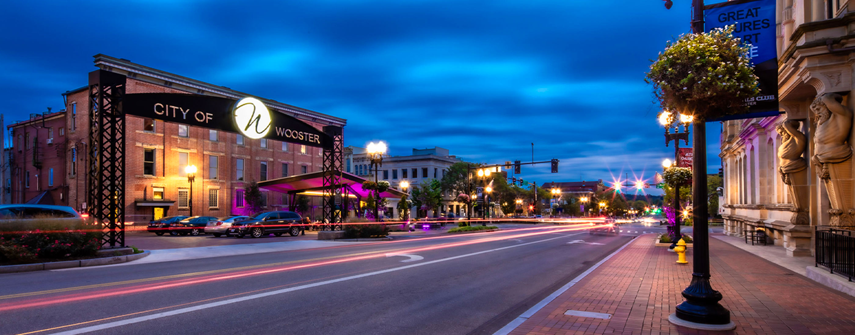 Cars drive through Downtown Wooster, Ohio streetscape at night.