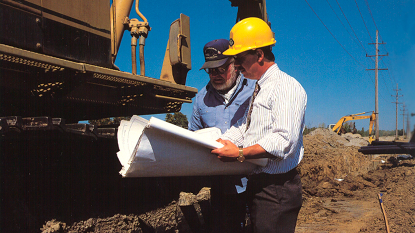 Two team members from OHM Advisors review plans at construction site.