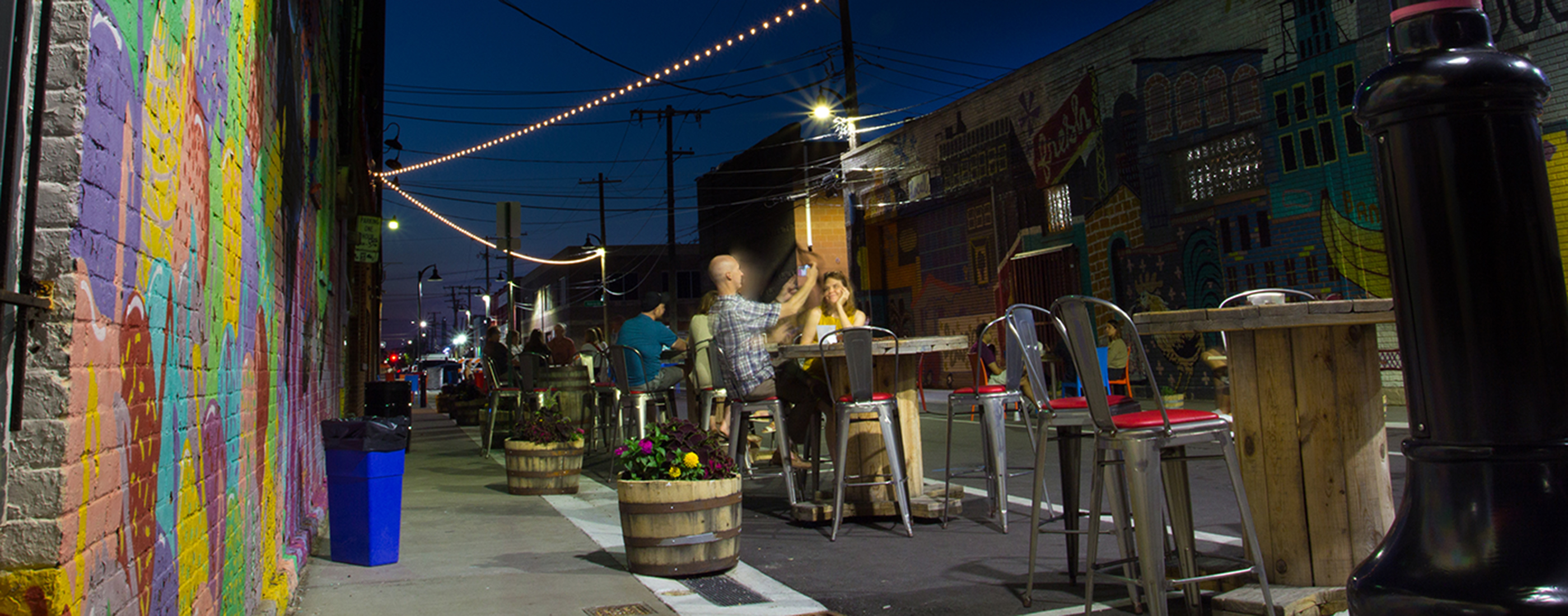 People sitting outside enjoying the new "flex" street with new lighting, seating, and streetscape.