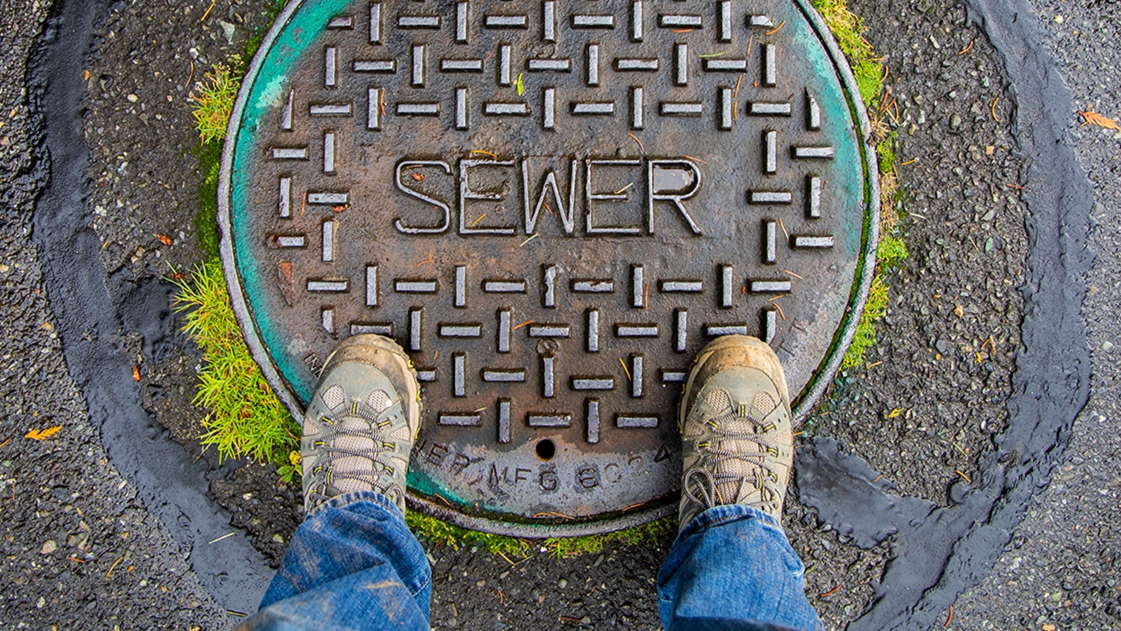 A asset management expert stands over a sanitary sewer cap.