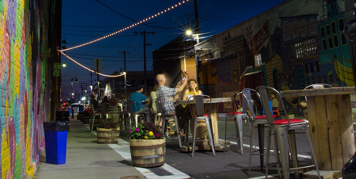 People sitting outside enjoying the new "flex" street with new lighting, seating, and streetscape.