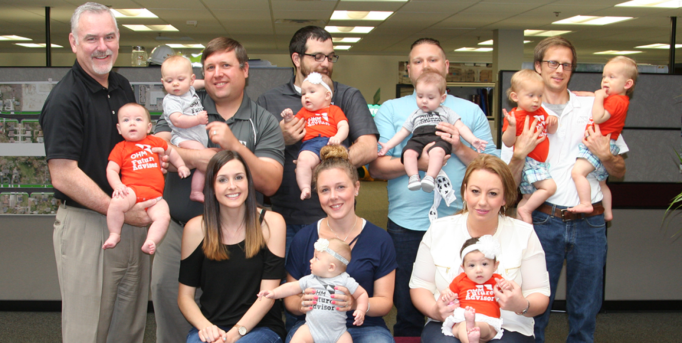 OHM Advisors' staff with their newborn babies, who show their flare in extra small OHM Advisors logo wear.