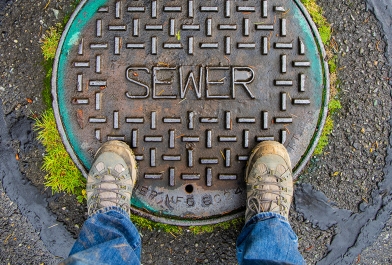 A asset management expert stands over a sanitary sewer cap.