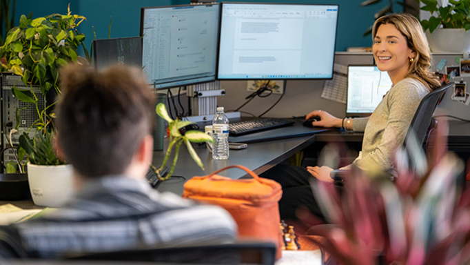 Two employees talking while sitting at their desks in an OHM Advisors office.