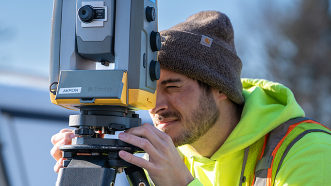 Surveyor with neon hoodie and safety vest looking into equipment lense.